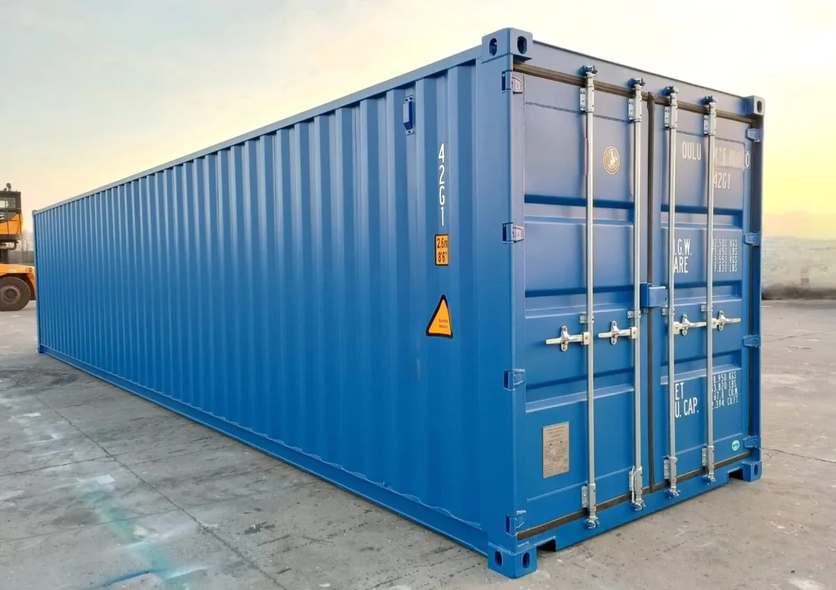 Blue 12m shipping container in good condition, photographed from the corner in a yard at sunset