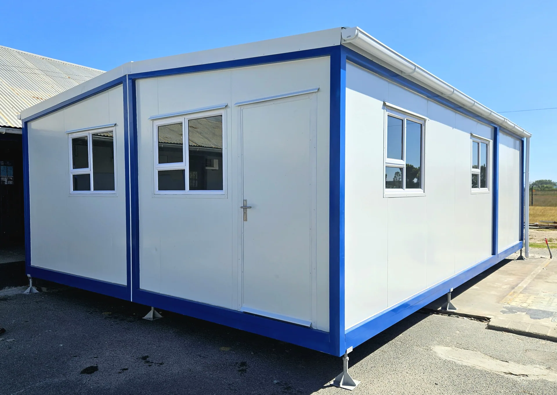 White modular classroom with blue trim, double doors and four windows, standing on levelling feet