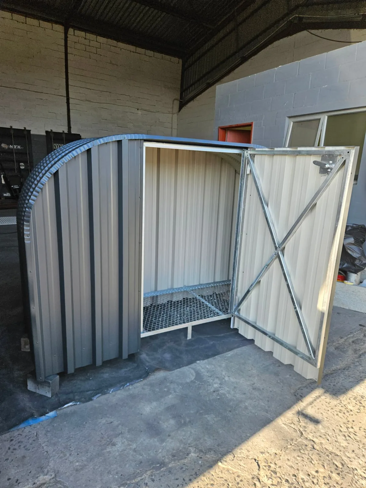 Angled view of a firewood shed with its lockable door open and cream corrugated interior lining