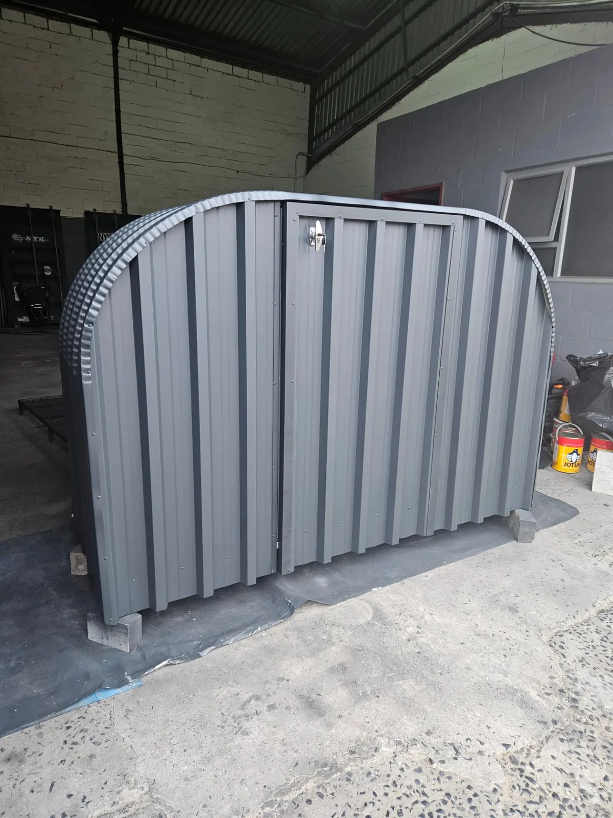 Front view of a grey firewood shed with closed lockable doors and stainless latch