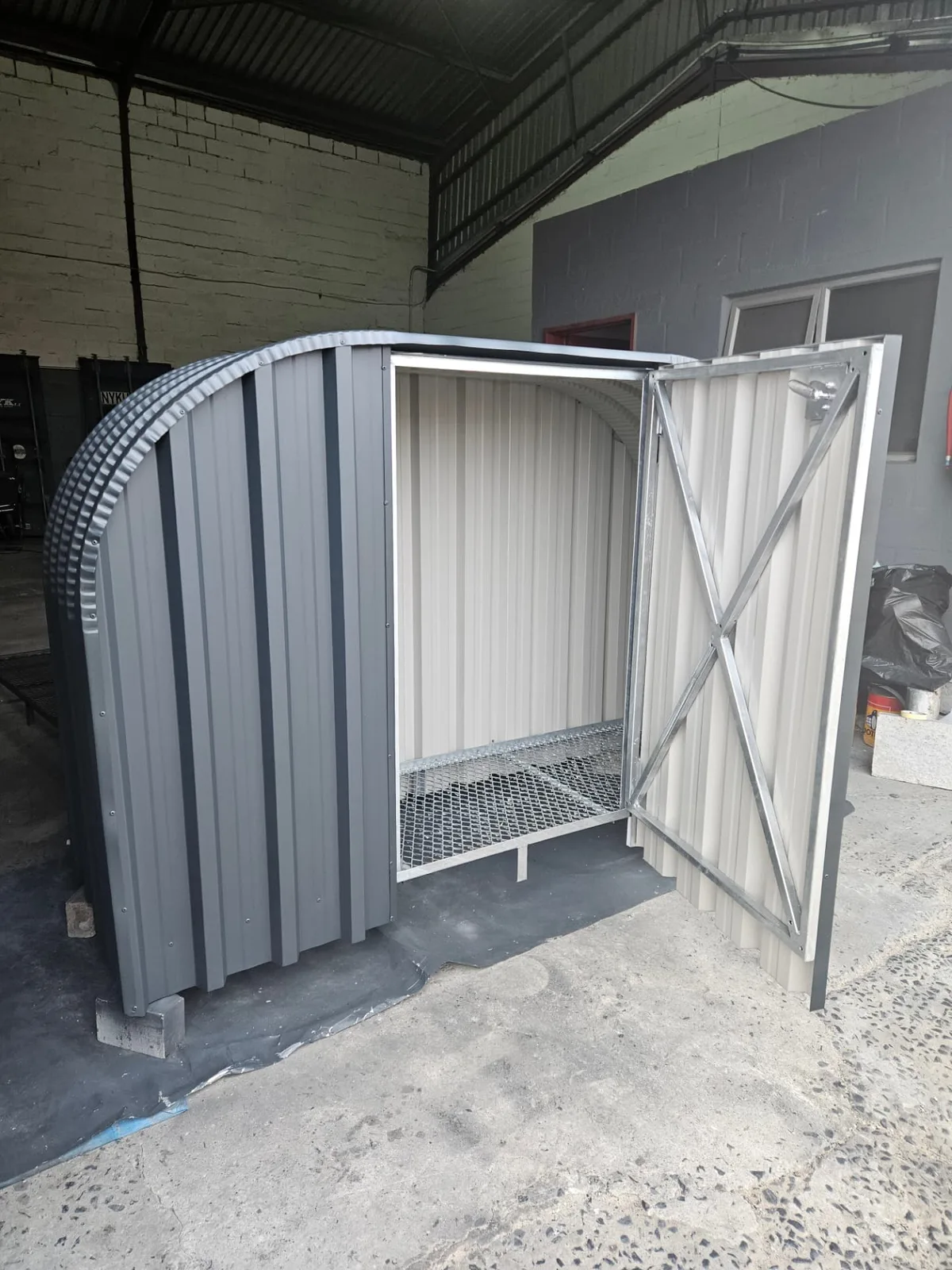 Grey firewood shed with the lockable door open, showing the cream lined interior and mesh base