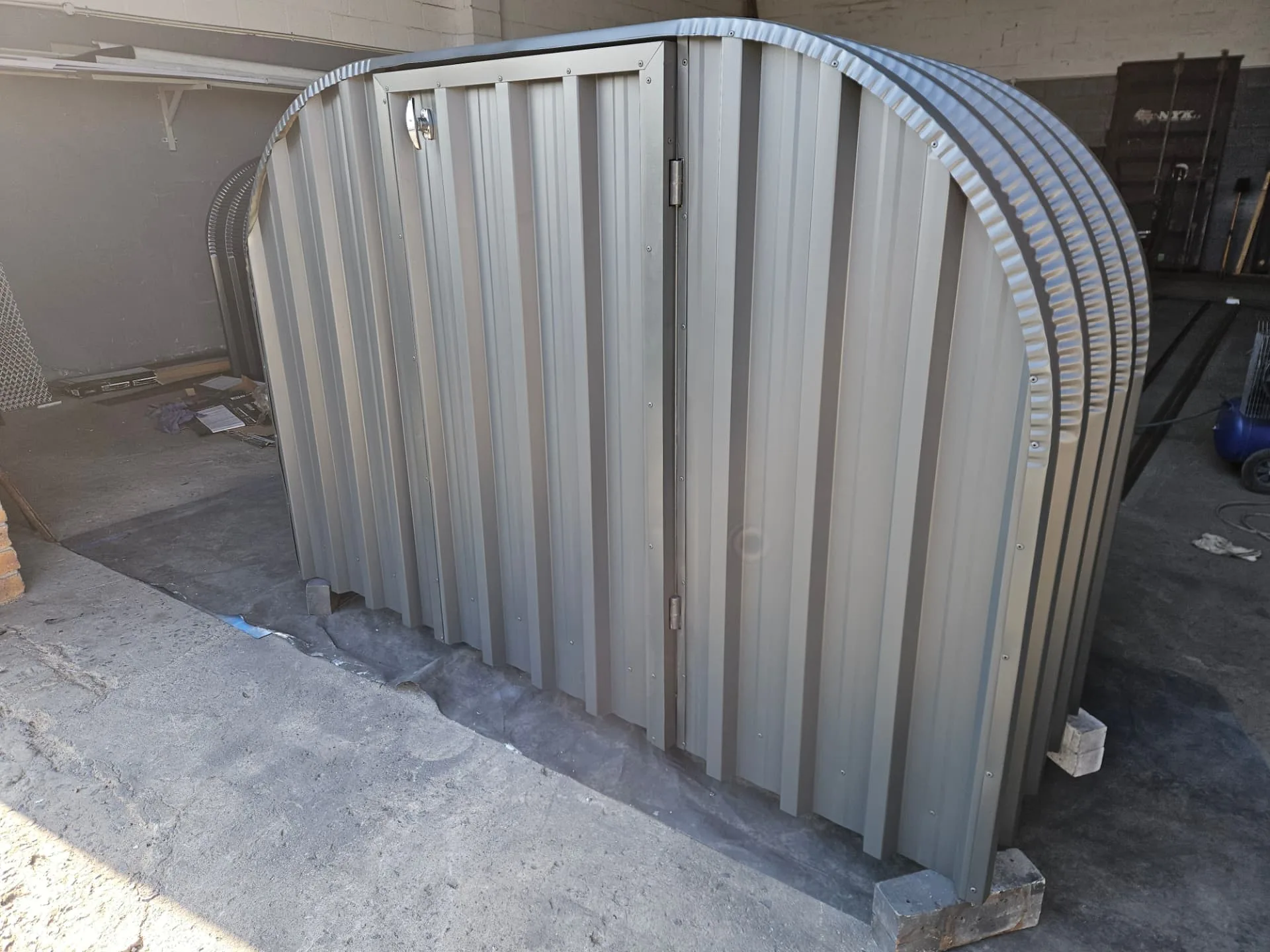 Firewood shed with closed cream steel lockable doors and a curved corrugated roof in the workshop