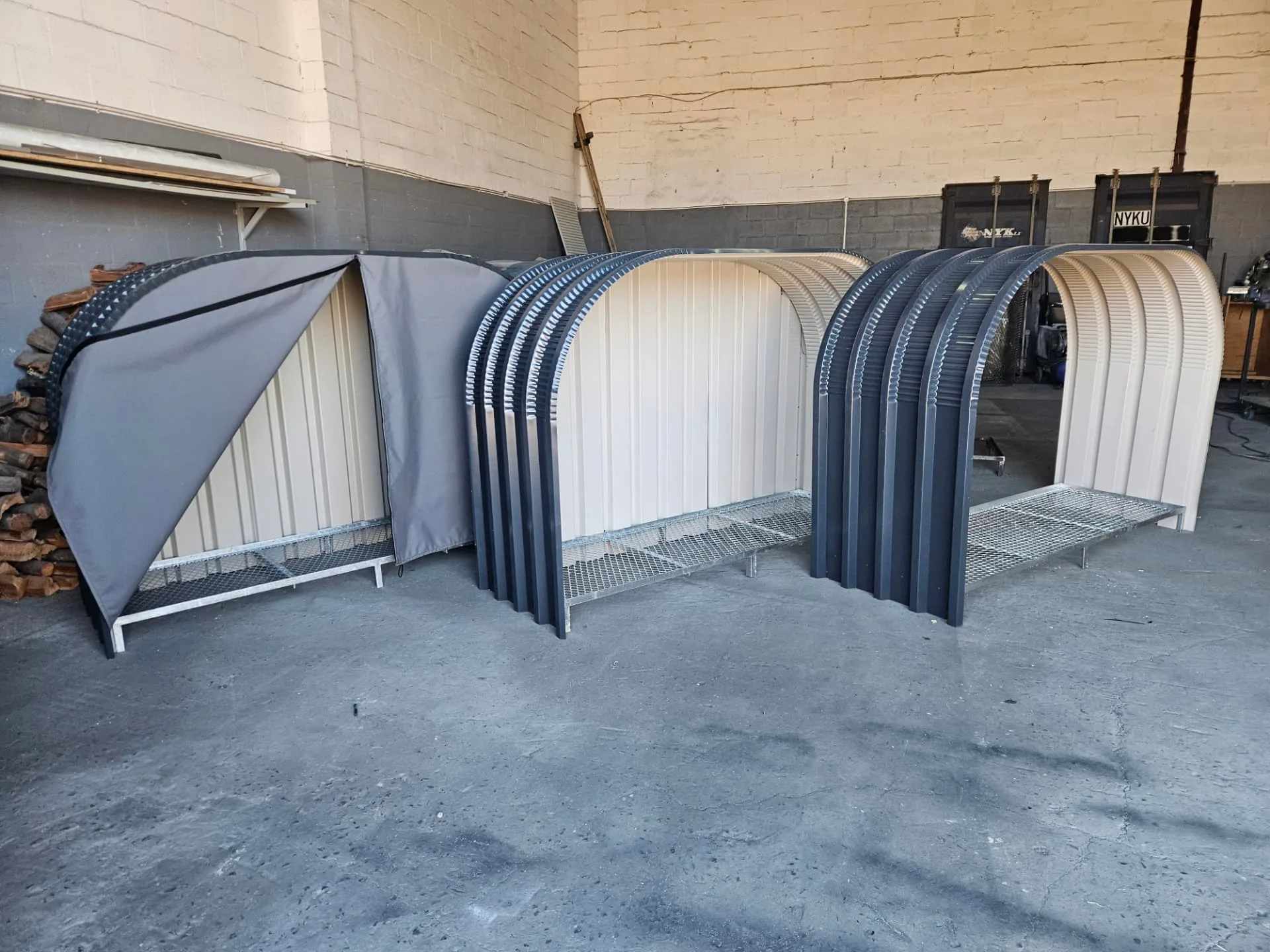 Firewood shed range in the workshop: canvas-covered unit, cream-backed unit and charcoal arch frame