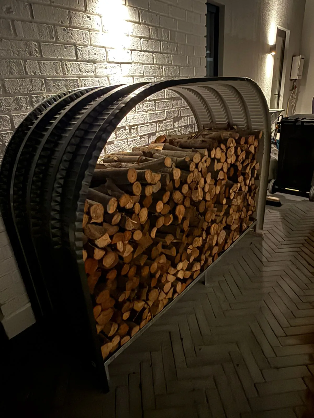 Firewood shed packed with stacked logs beside a white brick wall lit at night