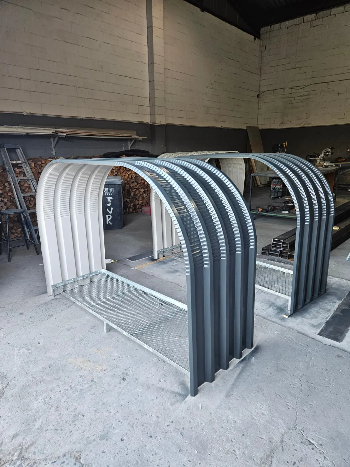 Three firewood shed frames in charcoal and cream at the workshop with galvanised mesh bases