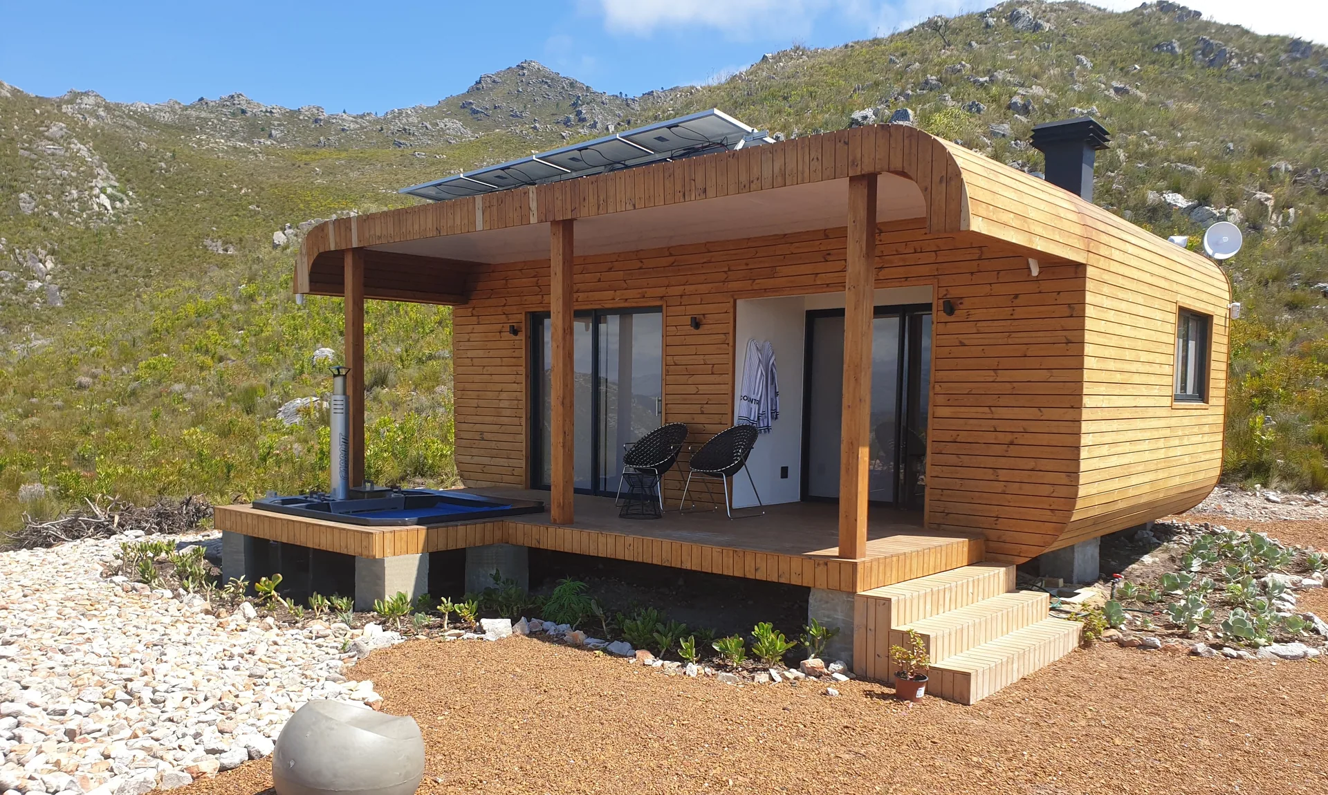 Timber-clad one-bedroom container house with veranda, plunge pool and roof-mounted solar panels against the mountains