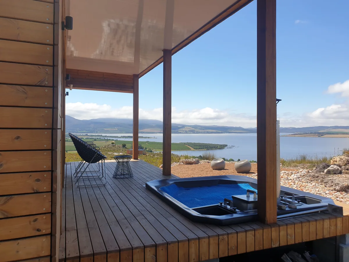 Covered container house veranda with a plunge pool and chair, looking across the water towards distant hills