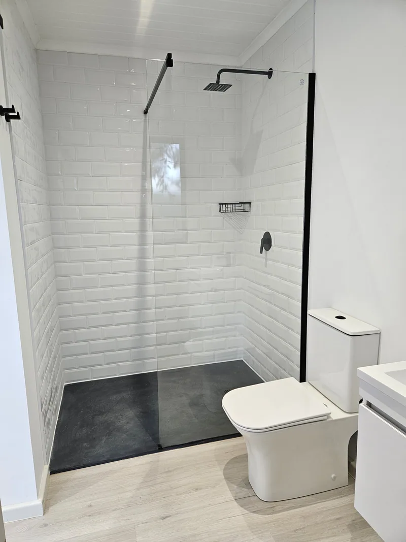 One Bedroom Pod bathroom detail showing the black-framed walk-in shower, dark floor tiles and white toilet