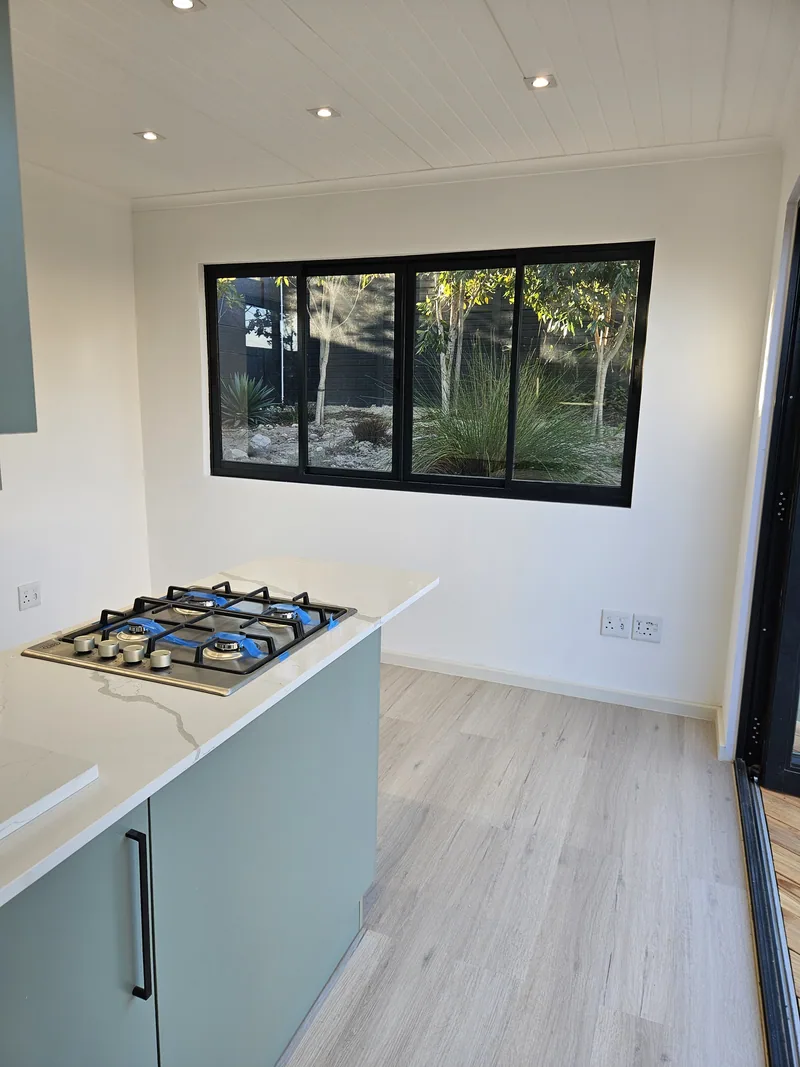 One Bedroom Pod kitchen island with gas hob, blue-grey cabinetry and black-framed window