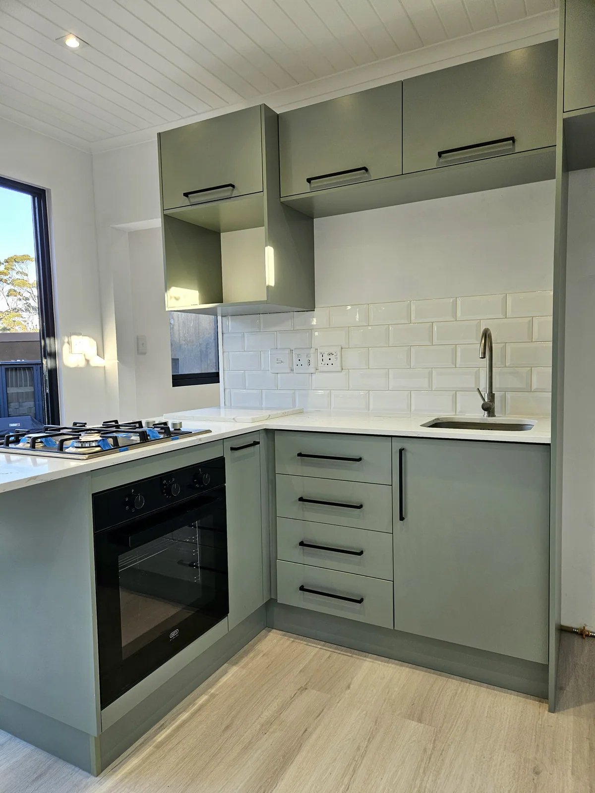 One Bedroom Pod kitchen with sage cabinets, tiled splashback, built-in oven and gas hob