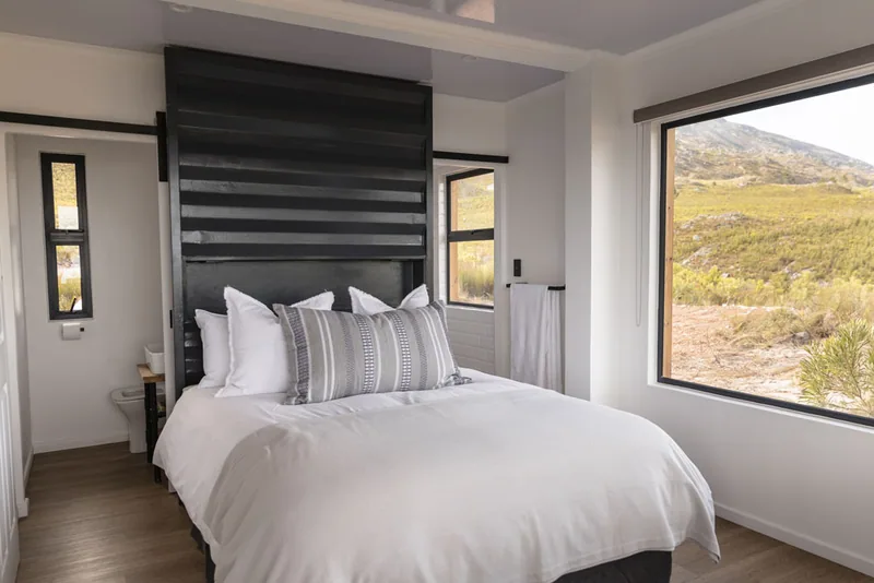 Bedroom with a double bed, black slatted headboard wall and a window looking onto open veld