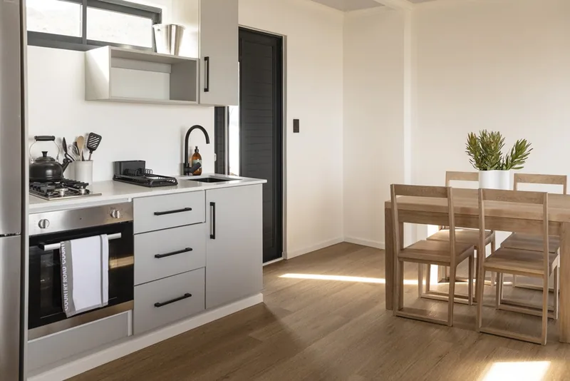 Kitchen with white cabinets, gas hob, built-in oven and an adjacent timber dining table and chairs