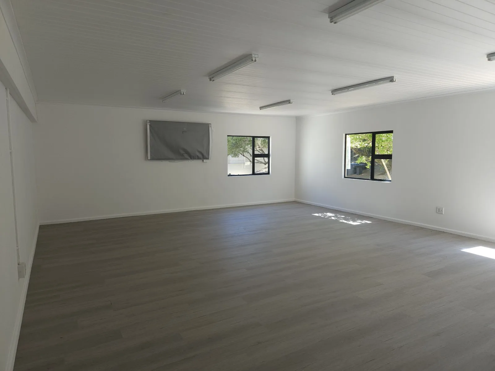 Empty art classroom interior with white walls, timber-look vinyl flooring and fluorescent light fittings