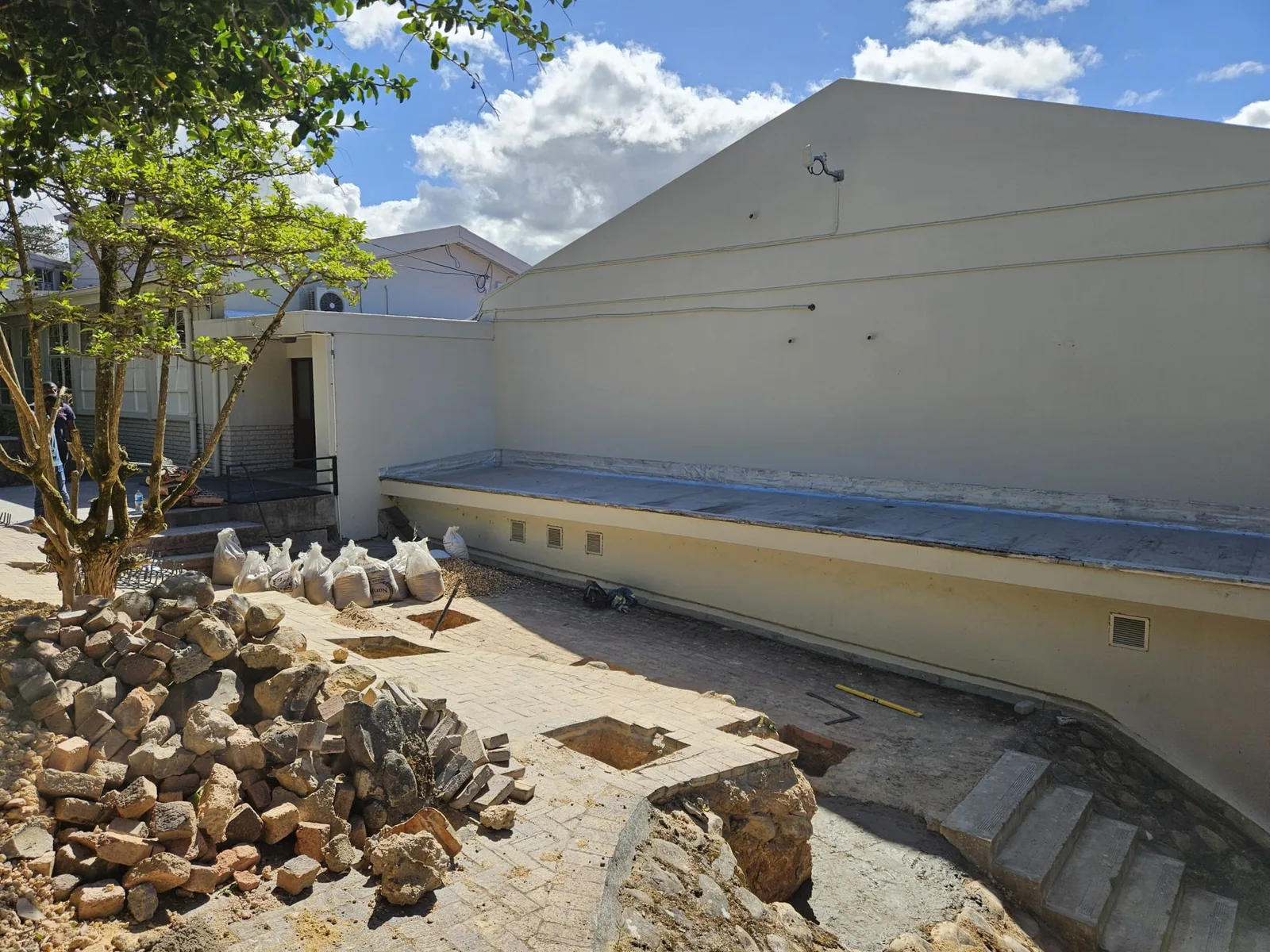 Site preparation before installation, with footings excavated in the paved courtyard beside the existing school building