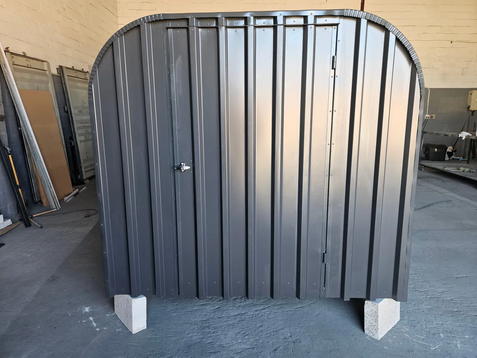 Front view of a charcoal arched bike shed with a lockable door, shown in the workshop before delivery