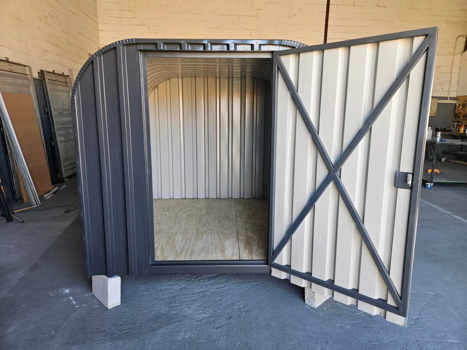Open lockable door revealing the empty interior of the bike shed with plywood floor and steel frame