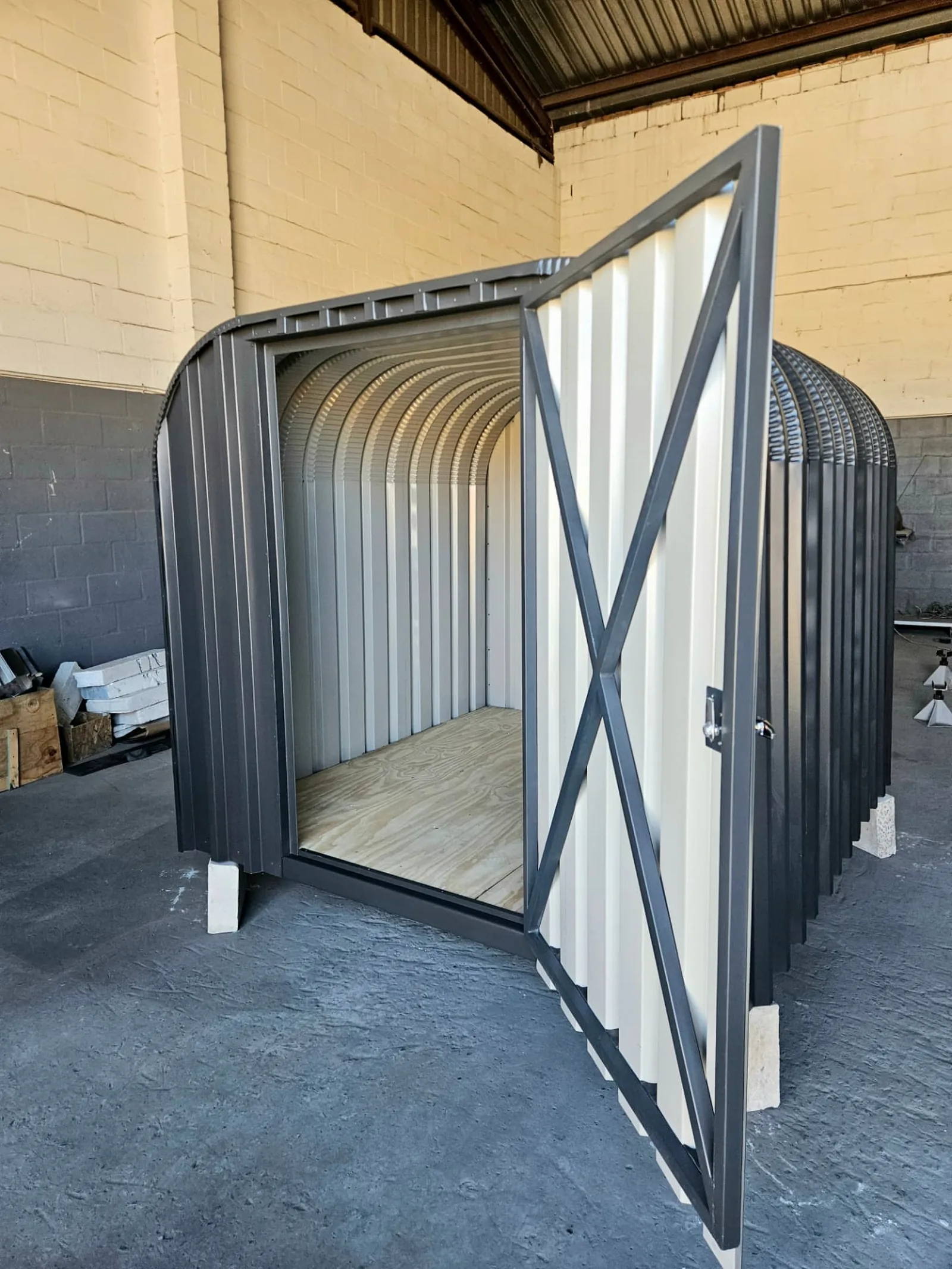 Interior view looking into the arched bike shed, showing the ribbed steel walls and plywood floor