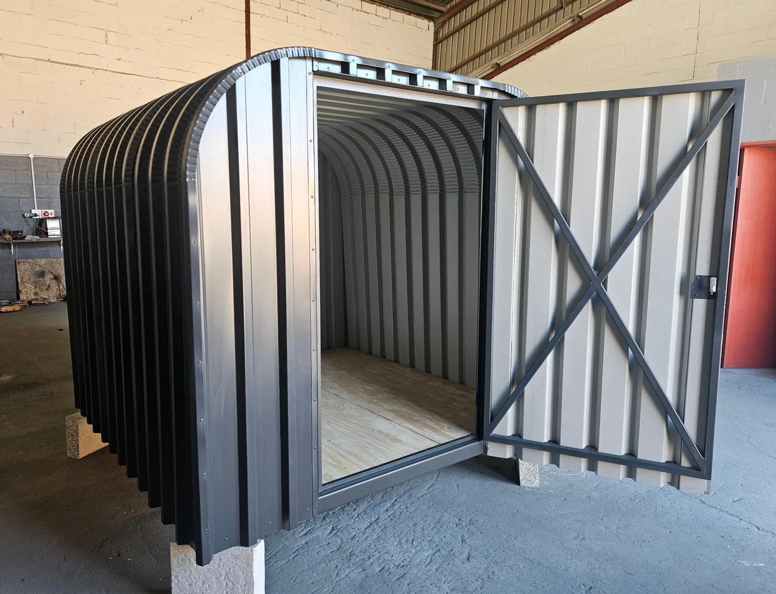 Open door showing the bike shed interior with plywood floor and light-coloured wall panels