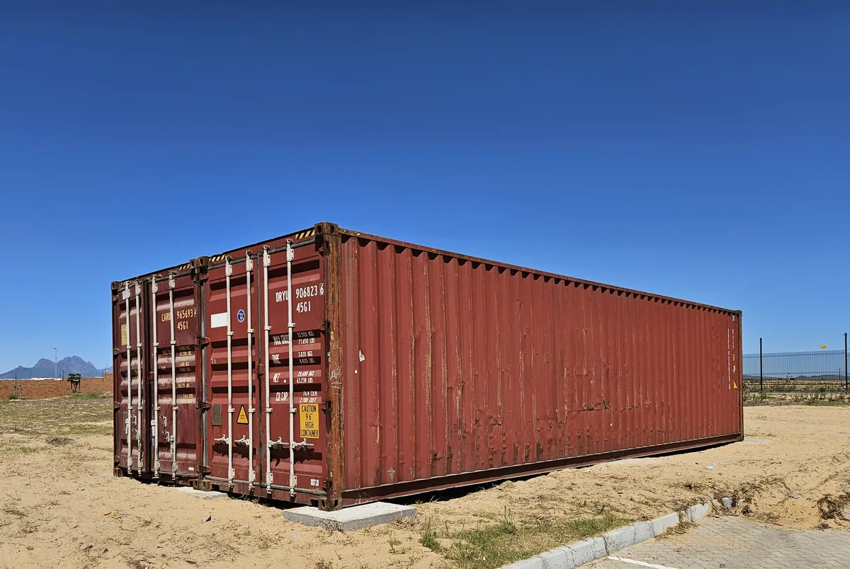 Rust-red shipping container standing on a sandy site with mountains on the horizon