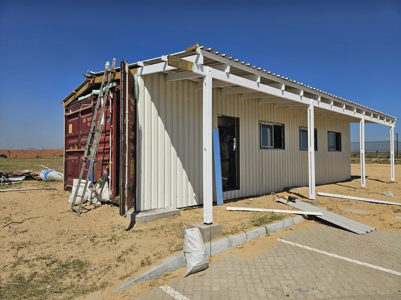 Container building part-clad in white IBR sheeting with a steel veranda frame erected along the front
