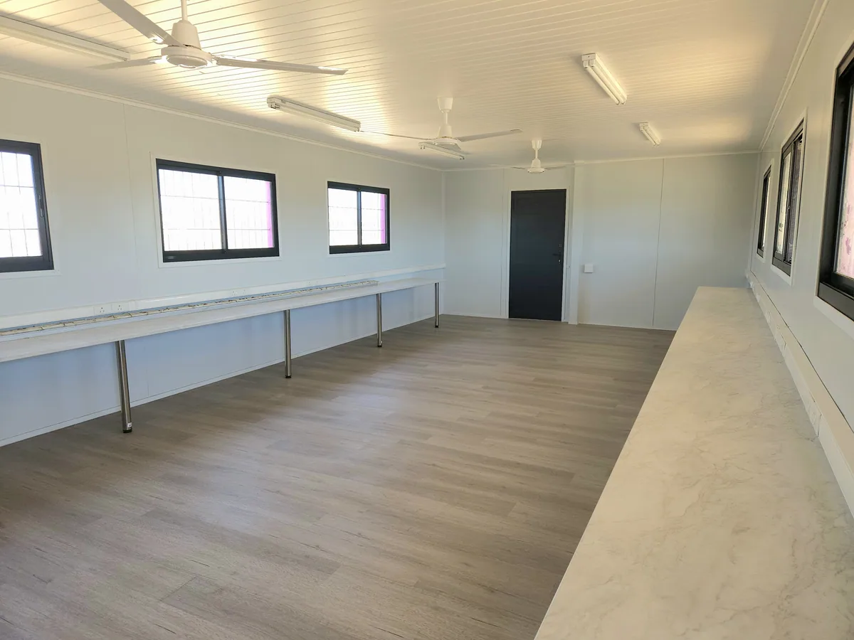 Classroom interior with wood-look flooring, white walls, ceiling fans and a long bench running down the room