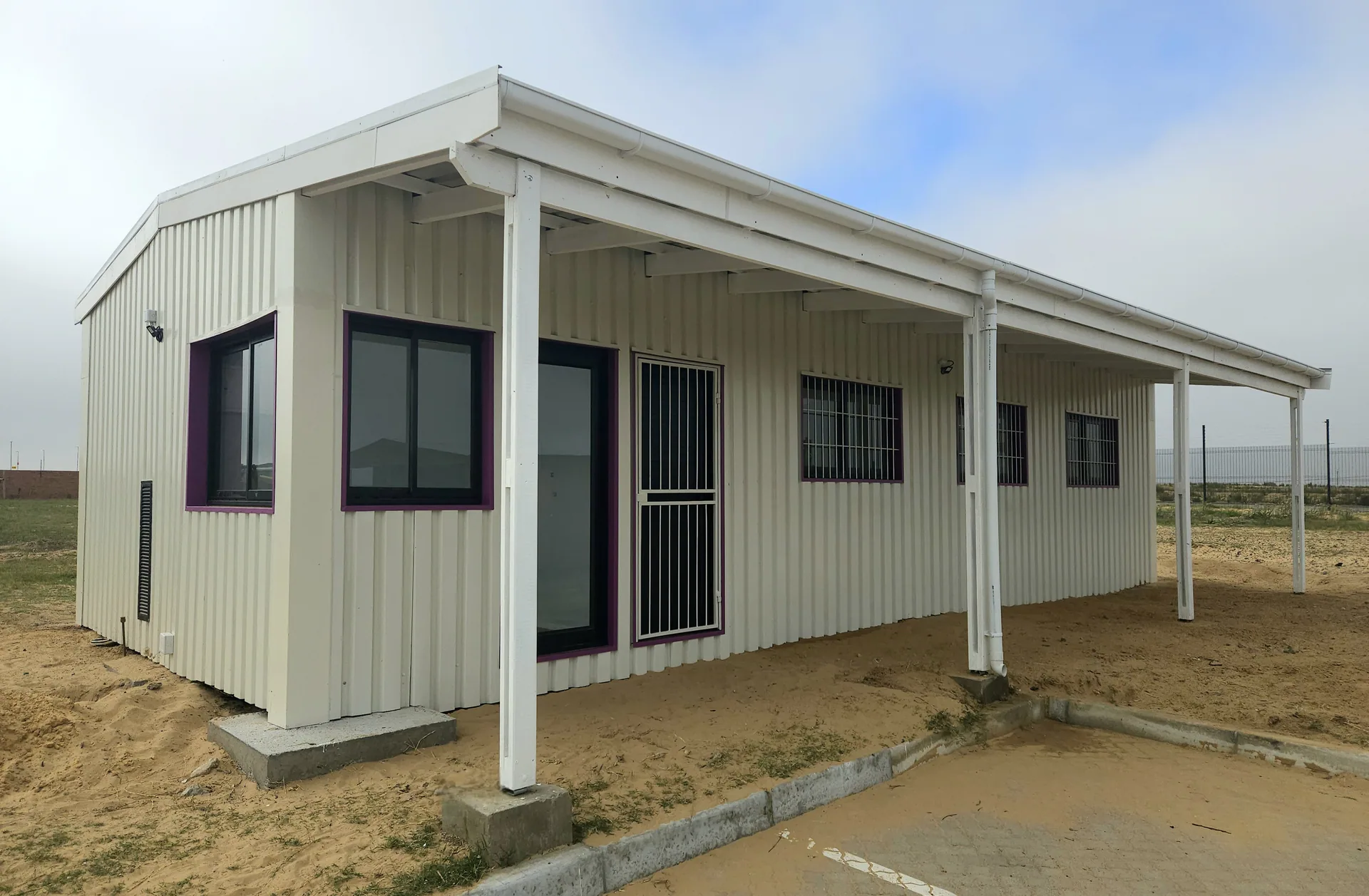 Completed white IBR-clad container building with pink window frames and a covered veranda along the front