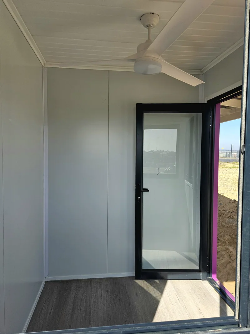 Interior corner of a classroom looking through a glazed door to the sandy site outside