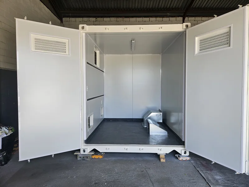 Interior of a white-lined container unit with both side doors swung open, showing a dark rubber floor and vents in the end wall