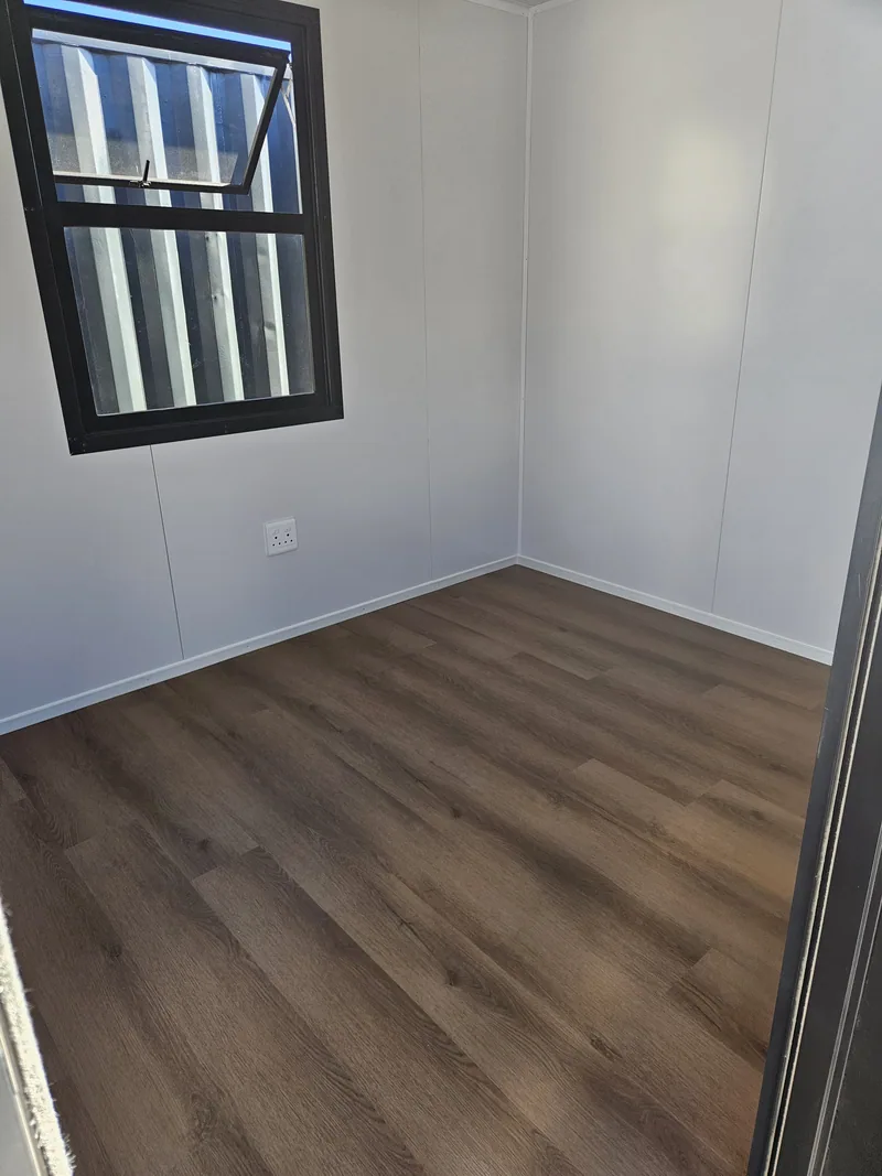 Empty office room with white walls, a black-framed awning window and dark wood-look flooring