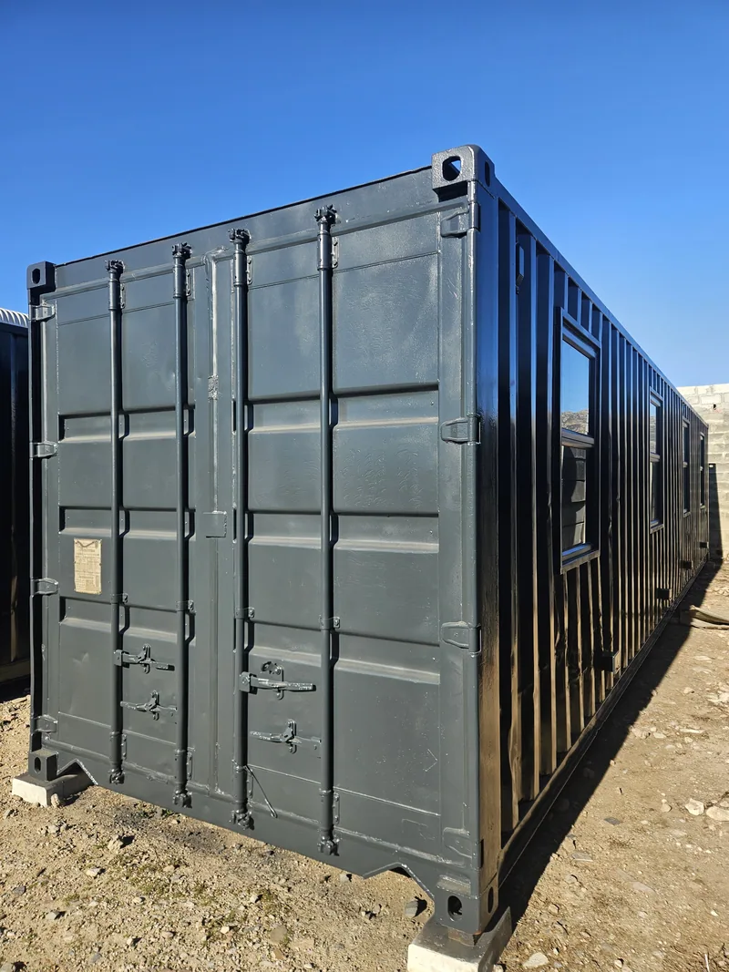 End view of a dark grey 12m container office standing on gravel under a clear sky