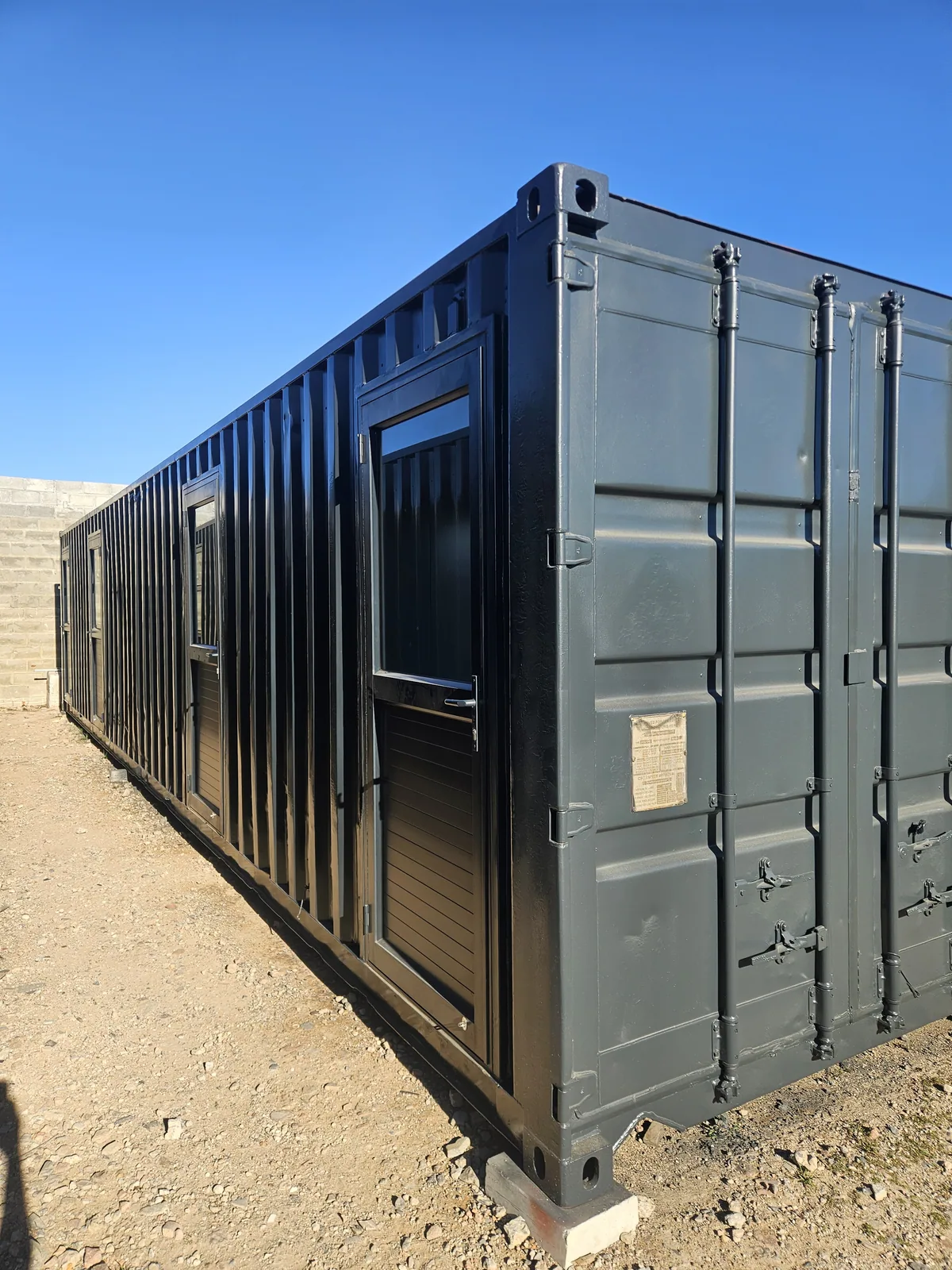 Angled view of a long dark grey container office with a personnel door and windows along the side