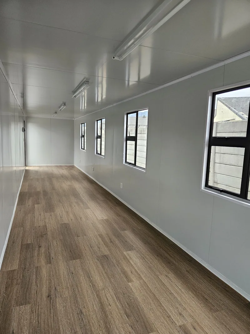 Open-plan container office interior with black-framed windows and light wood-look flooring