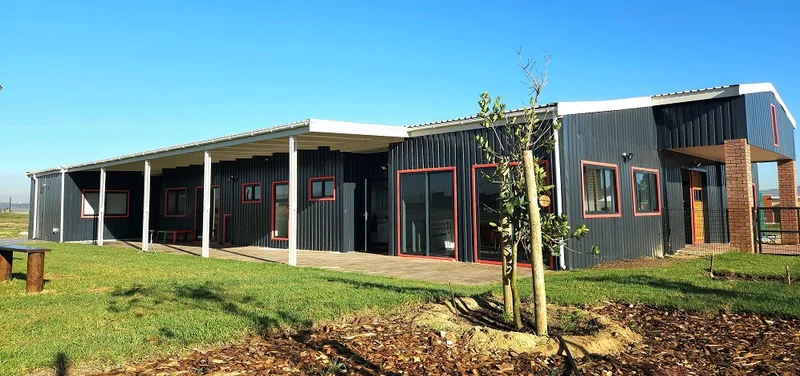 Completed early childhood development school exterior with covered walkway, red-framed windows and dark steel cladding