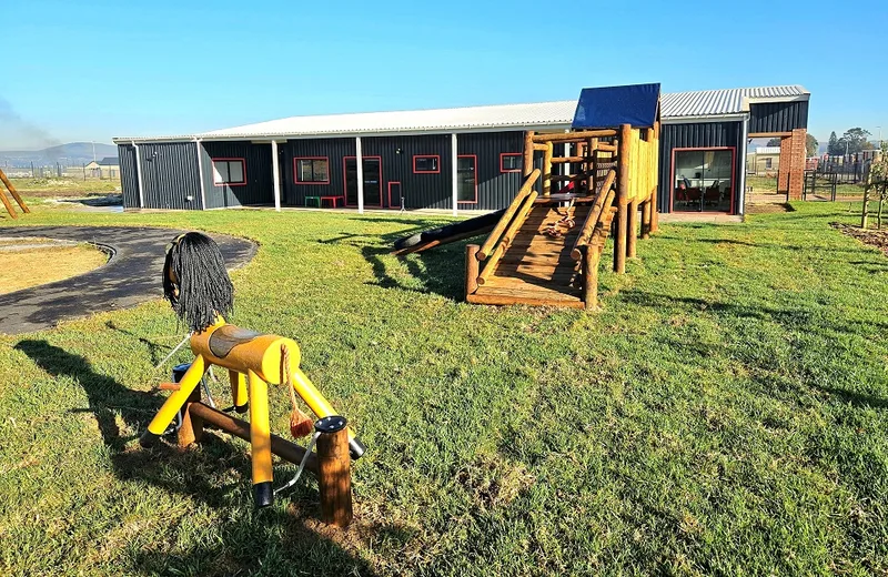 School building seen across the lawn with a timber jungle gym and play equipment in the foreground