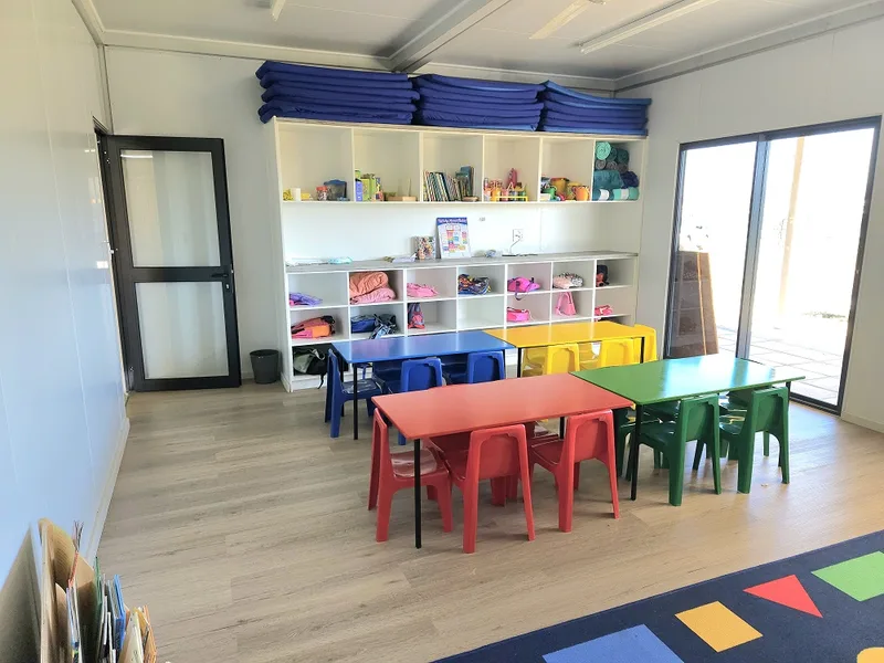 Classroom with colourful tables and chairs, open storage shelving and sliding doors to the outside