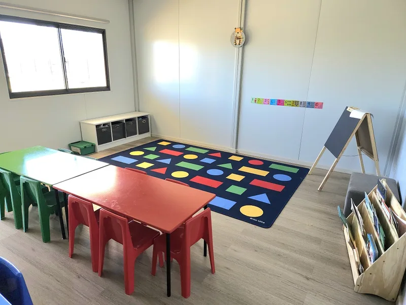 Classroom corner with a shapes rug, book display and low storage under a window