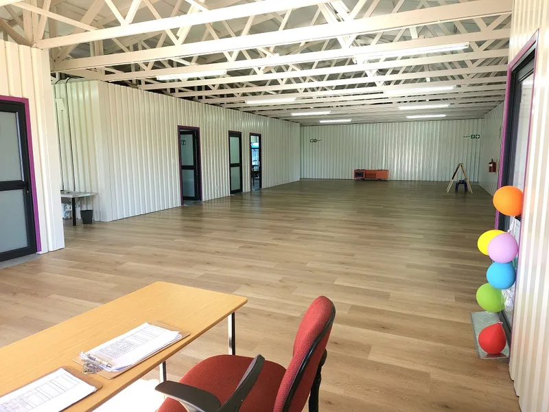 Large open hall with exposed steel trusses, timber-look flooring and full-height doors