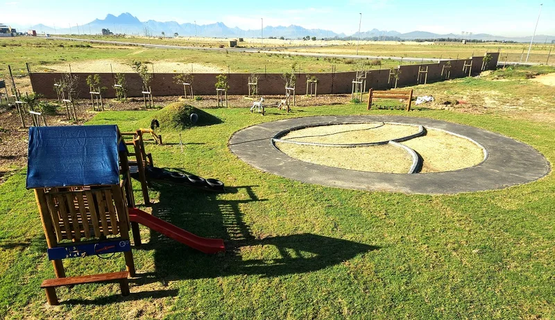 Outdoor play area with jungle gym, sand circle and mountain views beyond the boundary wall