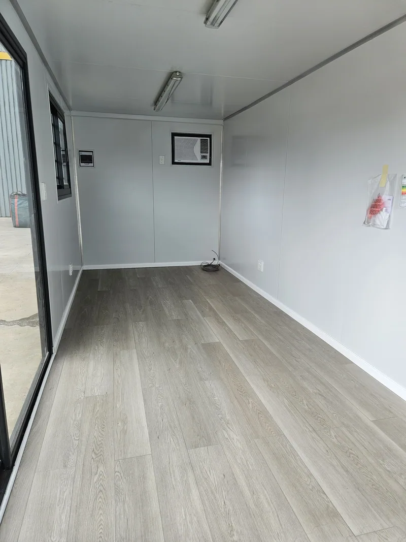 Empty container office interior with grey wood-look flooring, white walls and a glazed end wall