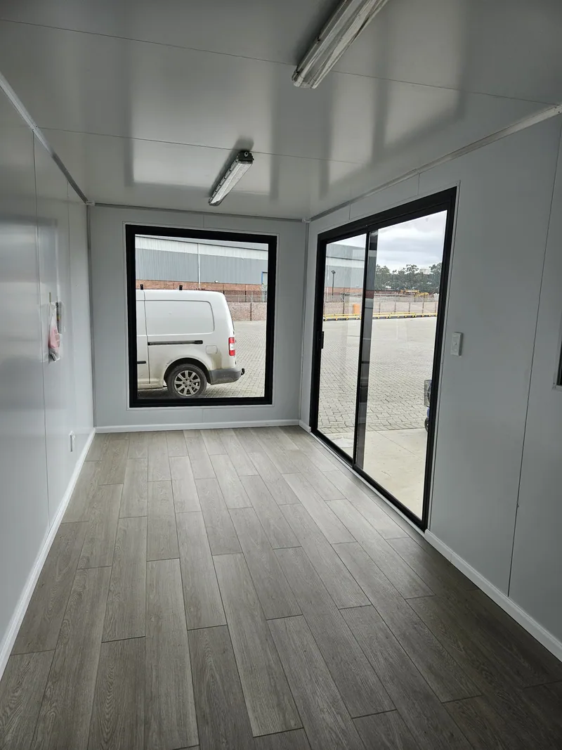 Container office interior looking out through glazed doors to a parked white van in the yard