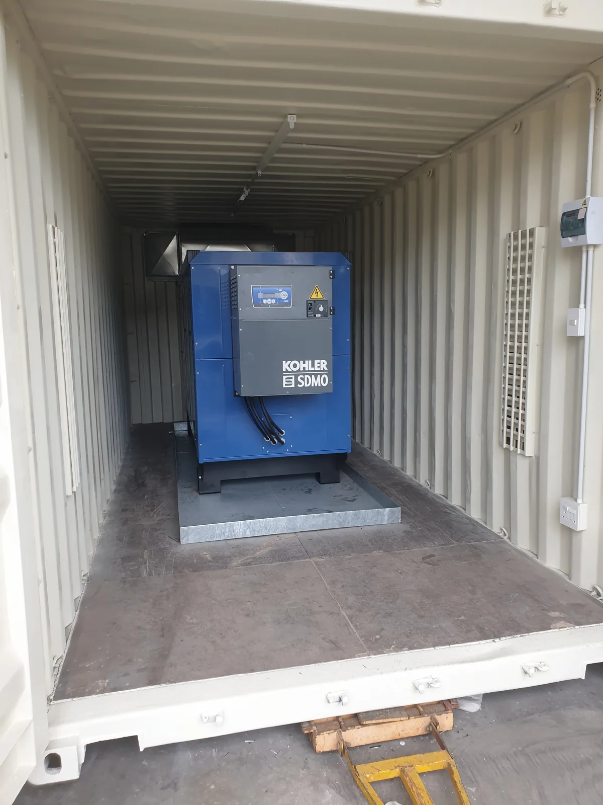 Blue diesel generator set installed on a plinth inside a white-lined container