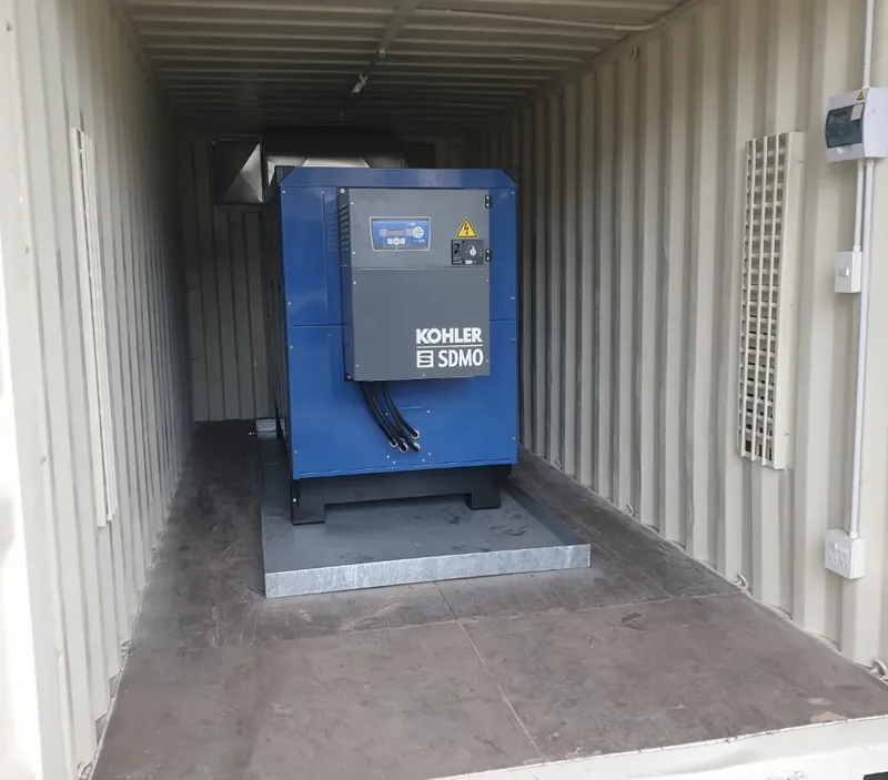 Blue generator set mounted on a concrete plinth inside a container with wall vents and control panels