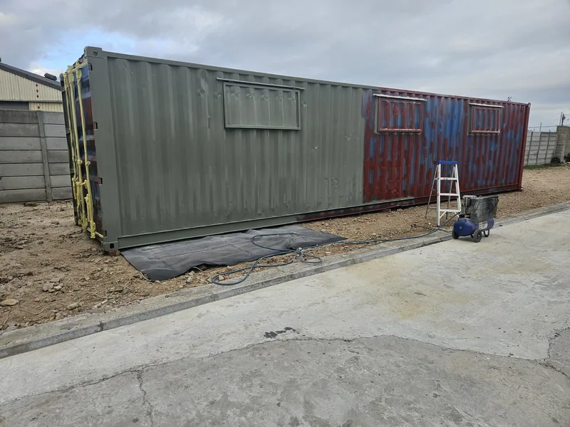 Green and red containers standing side by side on a construction site with a stepladder against the wall