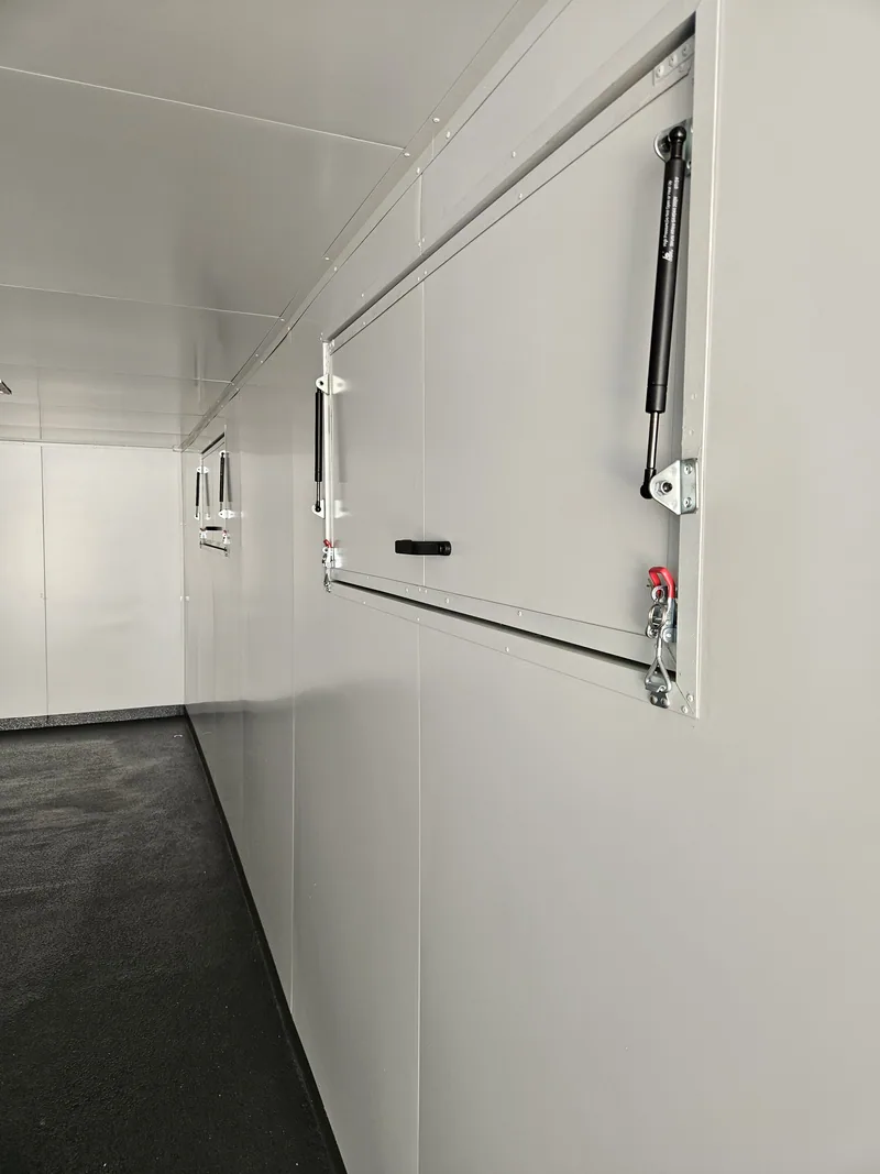 Interior of a white-lined container kitchen showing the gas-strut hatch mechanism and hinged panels