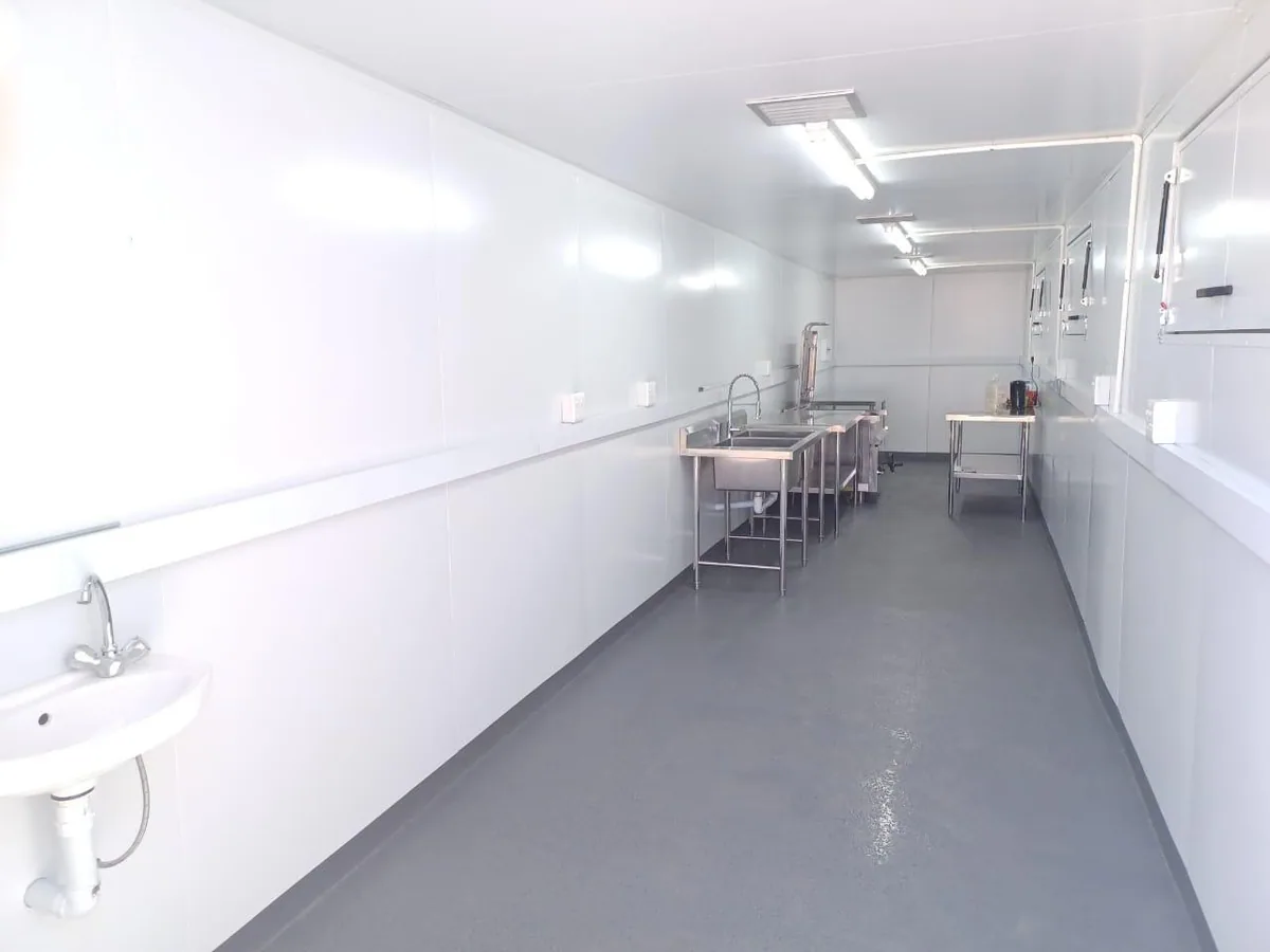 Long white-lined container kitchen interior with stainless prep tables, a wash basin and strip lighting