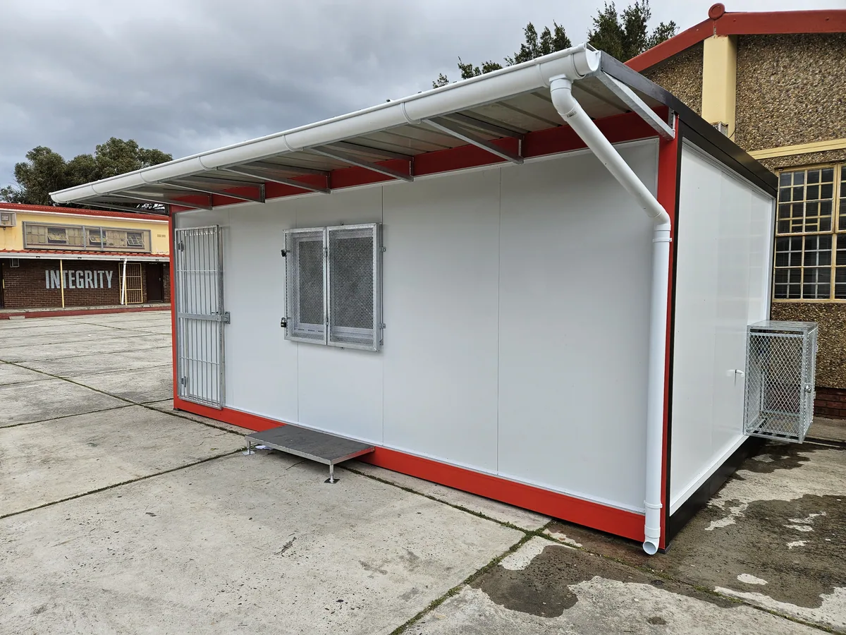 White modular kitchen unit with red trim and a projecting roof canopy, on a paved yard