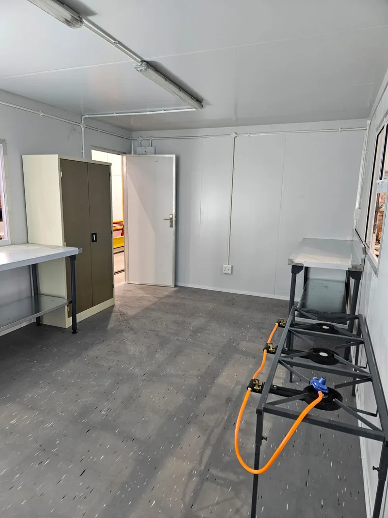 Interior of a modular kitchen unit during fit-out, with a stainless bench, cupboard and stepladder