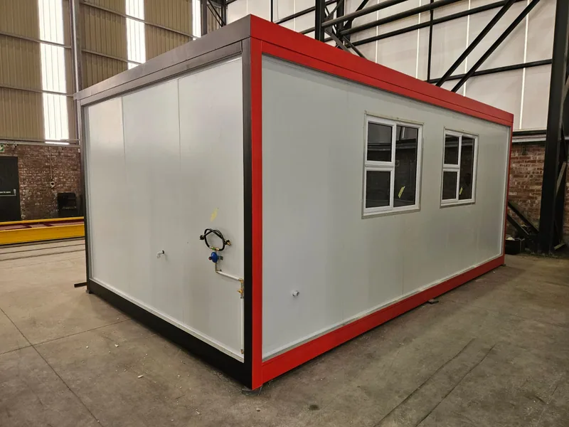 Modular unit with white cladding and red trim under construction inside a steel-framed workshop