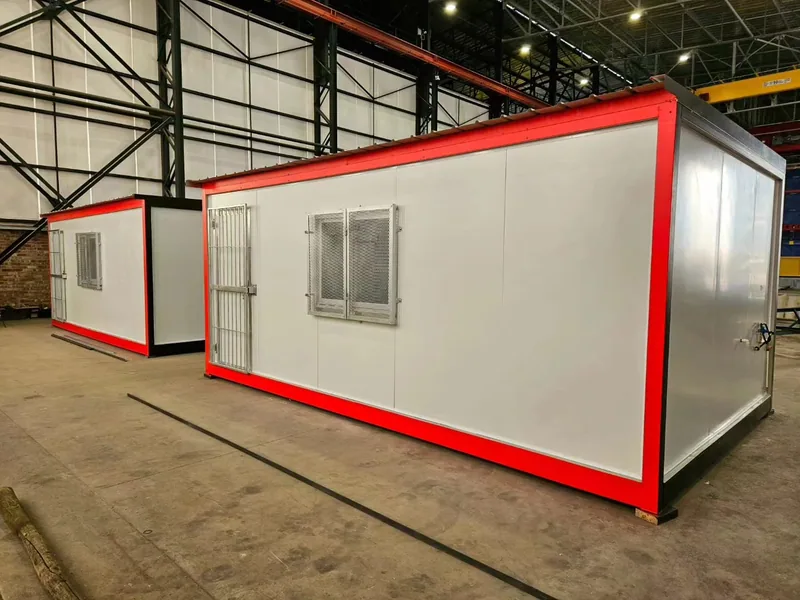 Two white modular kitchen units with red trim standing inside a fabrication workshop