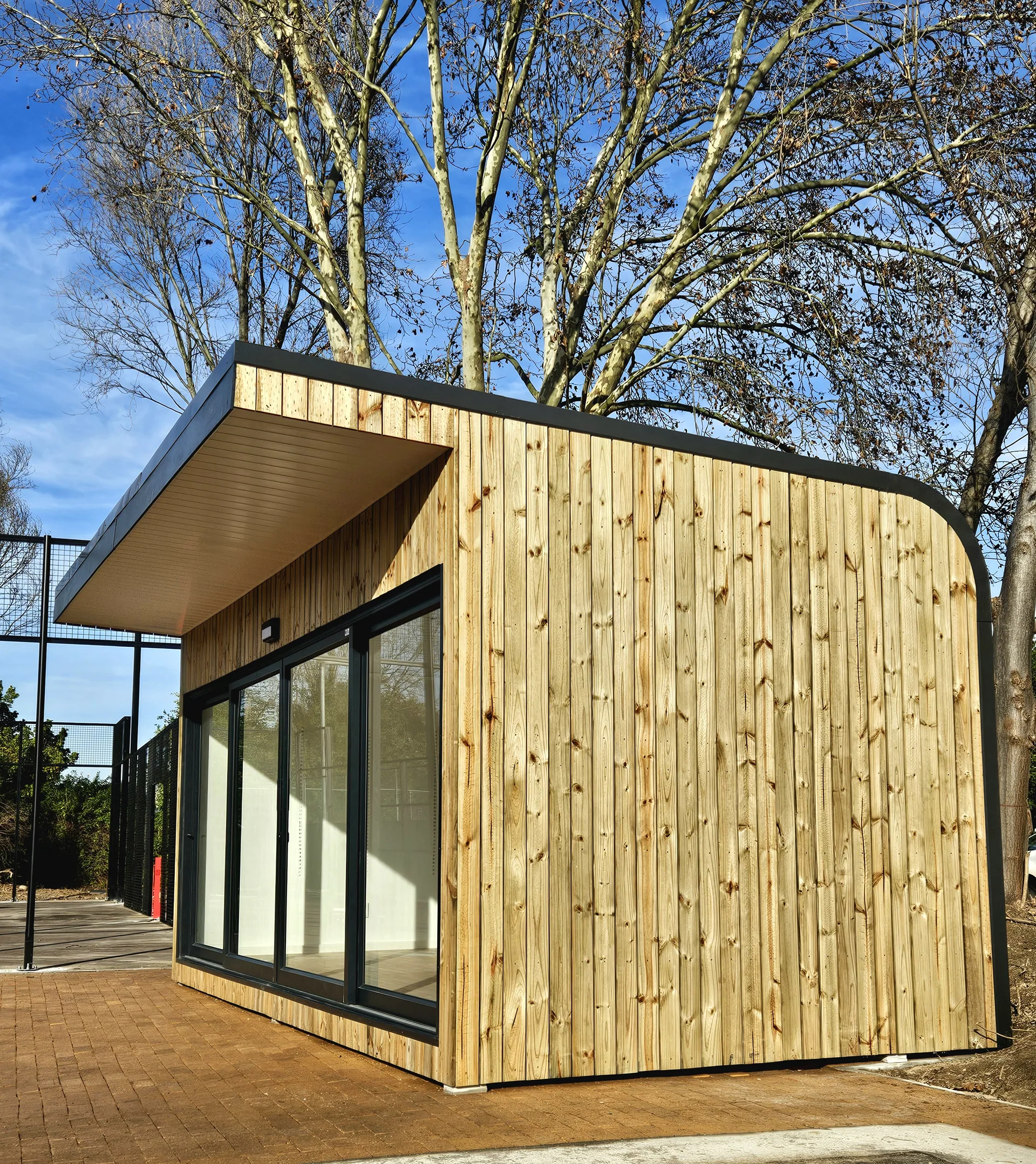 Timber-clad modular building with a curved cladding corner and large glazed frontage under bare trees